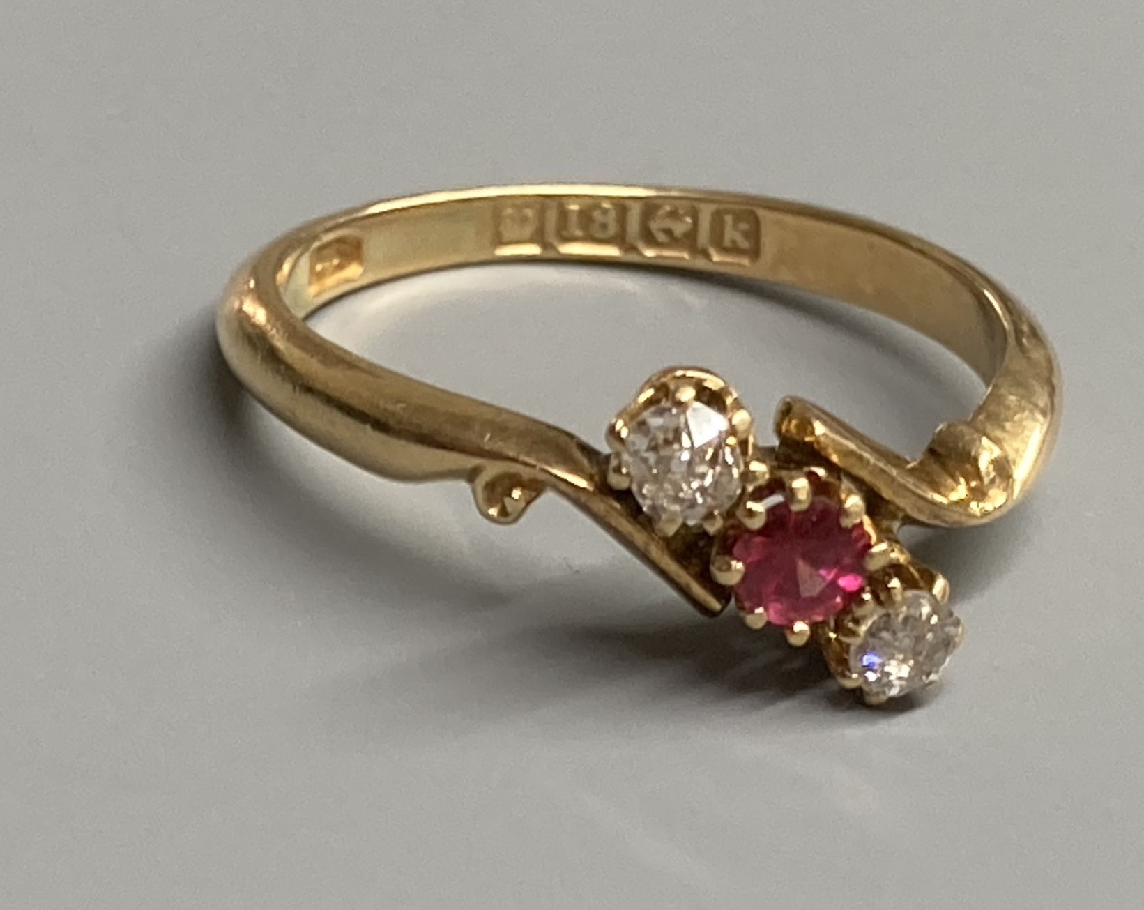 An Edwardian 18ct gold, red spinel and diamond set three stone crossover ring, size O, gross 2.9 grams